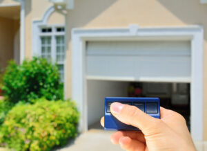 Emergency Garage Door Repair Brentwood TN A close-up view of a hand holding a garage door opener. In the background is a half-opened garage door.