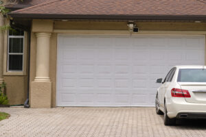 Vehicle parked in front of wide garage double door on paved driveway of typical contemporary american home.