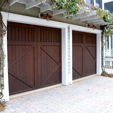 Two rustic wood garage doors installed on a home with a decorative pergola. 